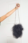 A person holding a Mongolian fur purse by its black chain against a white door background.