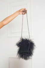 A person holding a luxury Mongolian fur purse with a feather trim and chain strap against a white door.