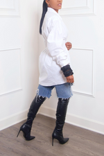 A woman wearing a white pleaded shirt, distressed Levi jean shorts, and black knee-high boots.