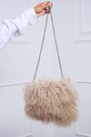 A woman holding a fluffy, beige Mongolian Fur Purse with a chain strap against a white door background.