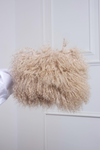 A person holding a voluminous, curly Mongolian Fur Purse against a white door 