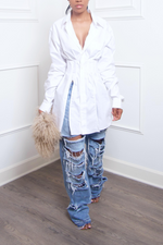 A person wearing a white dress, heavily distressed denim jeans, and blue open-toe slippers, holding a Genuine Mongolian Fur Purse, standing against a white wall.