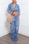 Woman standing wearing a unique piece, Denim Asymmetrical Jean Jacket, heavily distressed jeans, and holding a furry handbag.