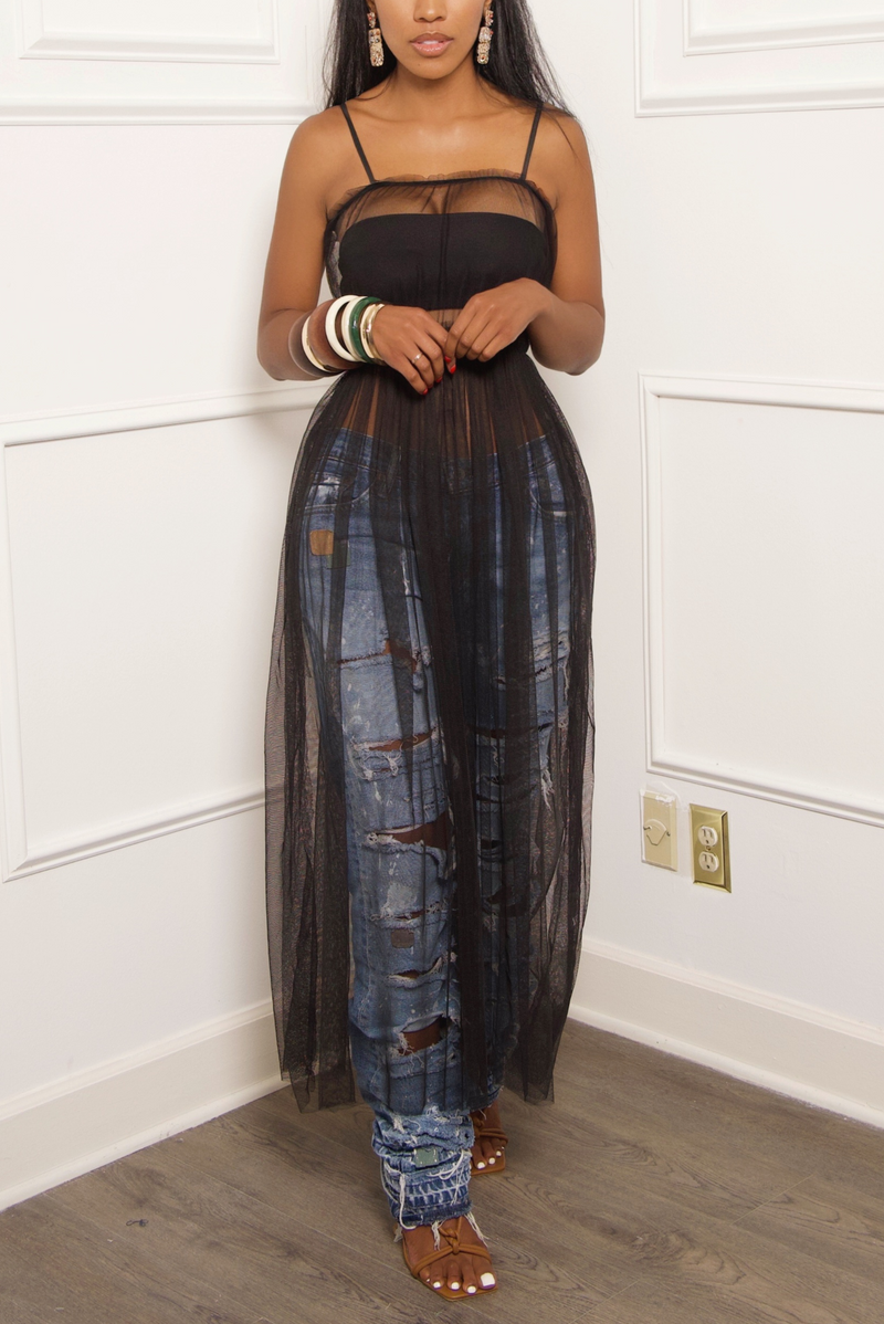 A woman standing wearing the Black Sheer Tulle Maxi Dress with ripped jeans and bangles.