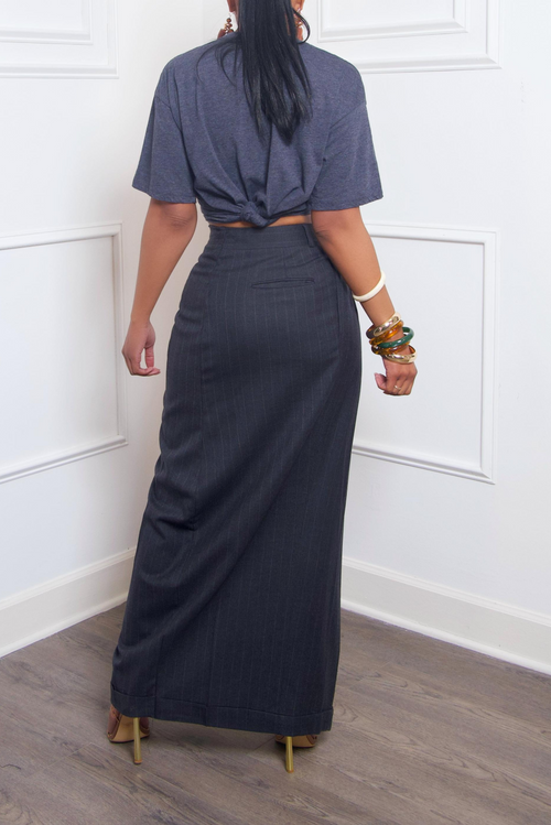 A woman from behind, wearing a gray knotted t-shirt and an Off Black Long Pinstripe Slacks Wrap Skirt with high heels.