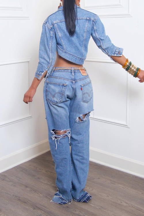 A woman wearing an upcycled denim outfit with heavy rips and frayed edges, standing in front of a white door.