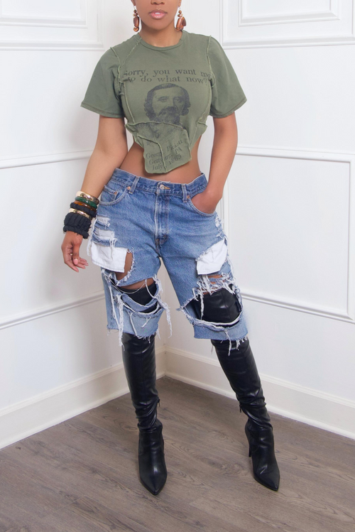 A woman stands wearing a cropped green t-shirt, upcycled distressed Levi Jean Shorts, and black knee-high boots.